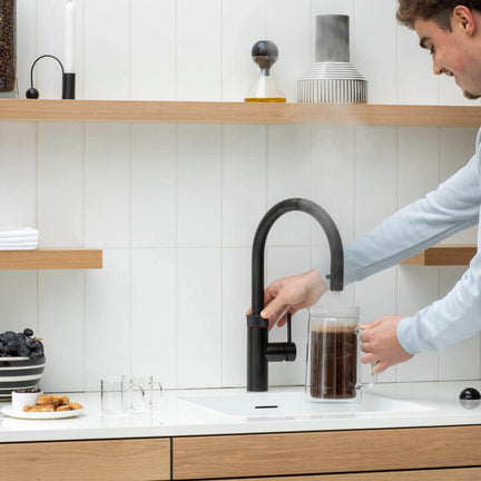 5 gode grunner til å velge en Quooker, en mann tapper kokende vann i kaffekannen fra sin Quooker Flex svart matt kran